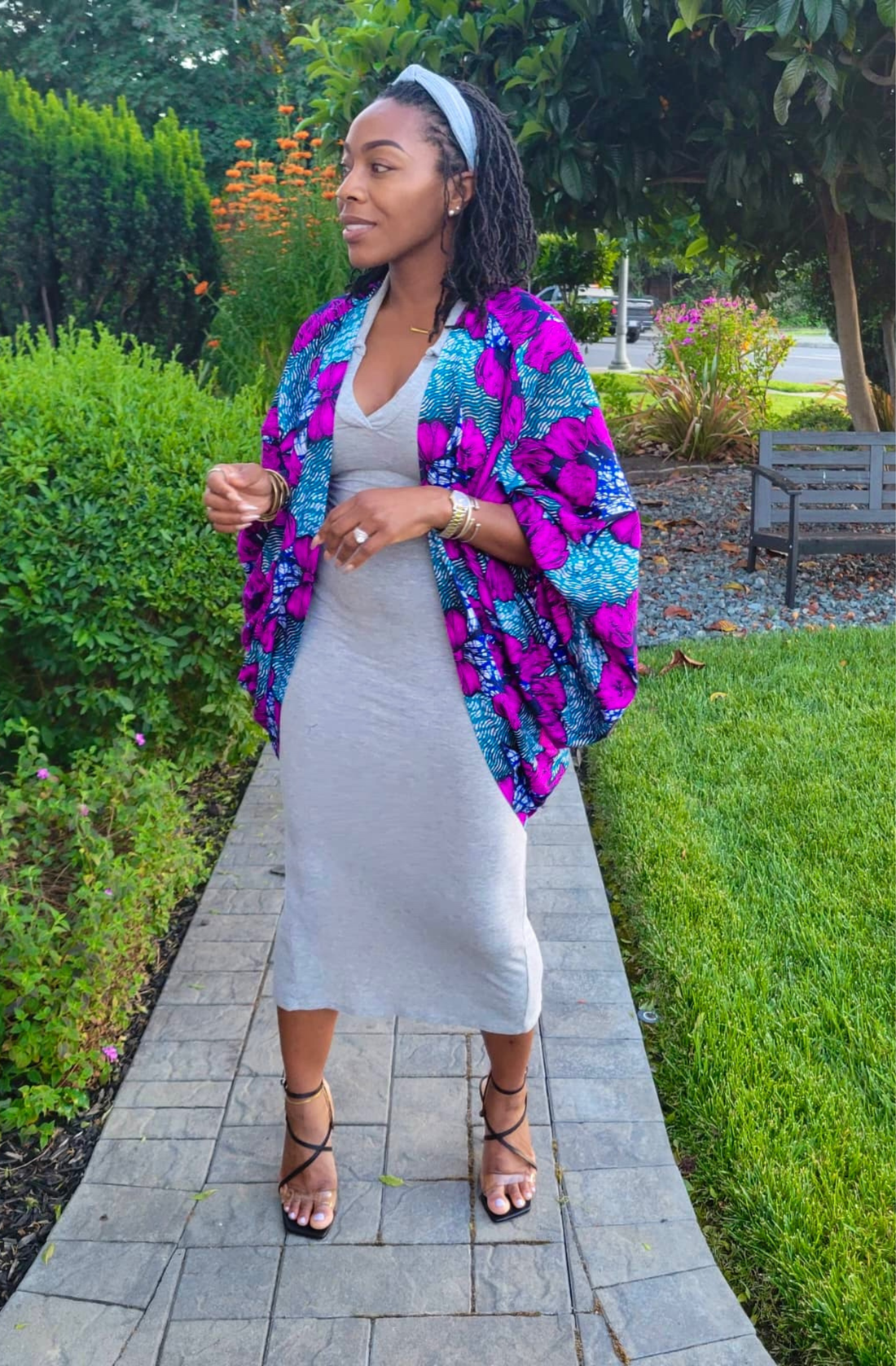 Woman in a colorful jacket and white dress standing on a garden path.