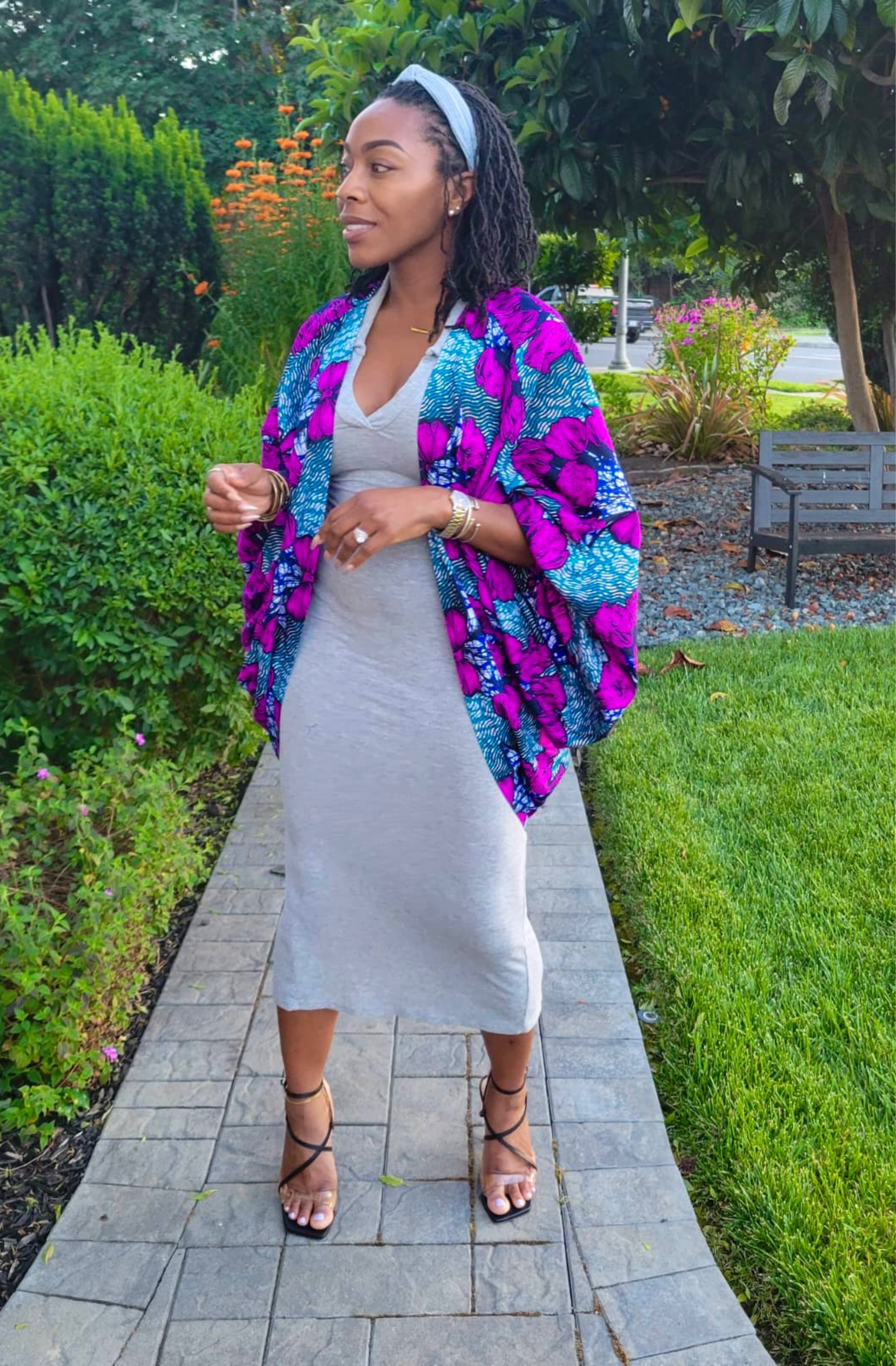 Woman in a colorful jacket and white dress standing on a garden path.