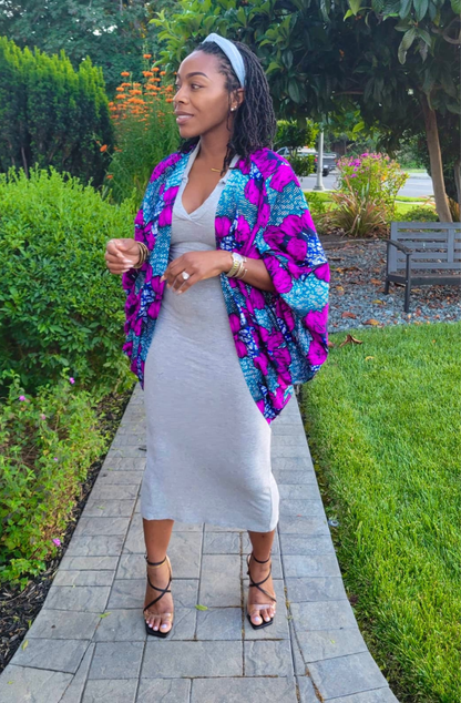 Woman in a colorful jacket and white dress standing on a garden path.