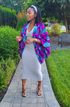 Woman in a colorful jacket and white dress standing on a garden path.